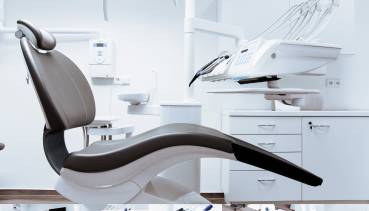 A collage of images showcasing a modern dental clinic room. The central image features a dental chair with an overhead lamp in a clean, white room with dental equipment on the side. The surrounding images provide close-up views of the dental instruments, sink, and other sterilized tools used for dental procedures, emphasizing the clinic's high standards of hygiene and organization.
